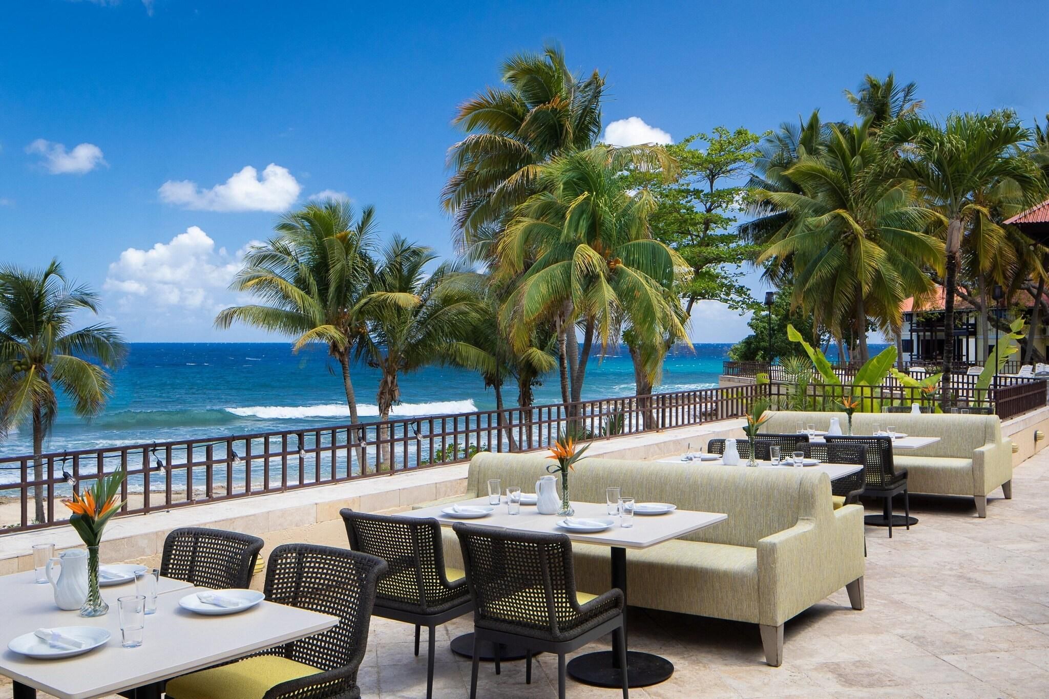 A seaside restaurant with outdoor seating, palm trees, and ocean views.