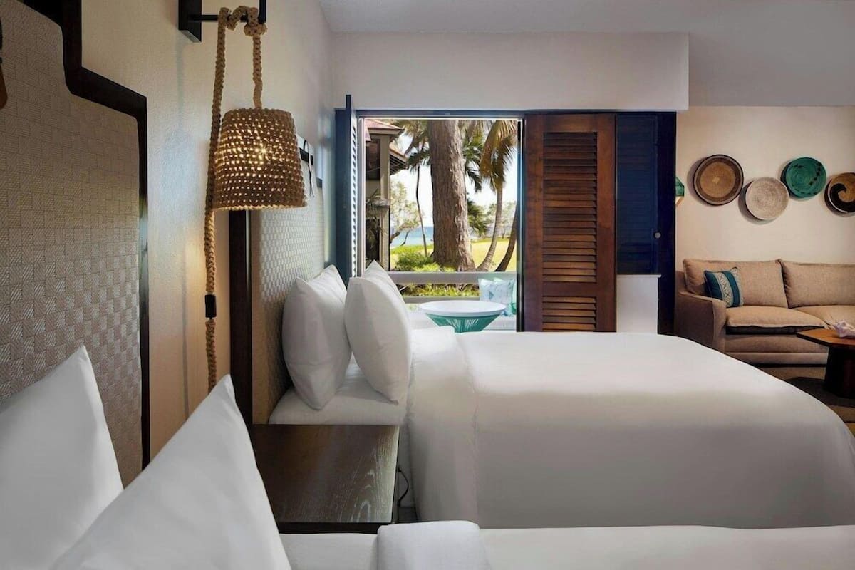 Habitación de hotel con cama, sofá, lámpara colgante y vistas al exterior.