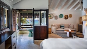 A modern hotel room with a balcony, a sofa, a bed, and a TV. - Carambola Beach Resort (Kingshill)