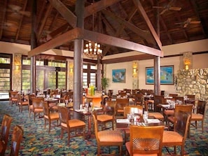 A spacious dining area with wooden tables and chairs, stone walls, and large windows.