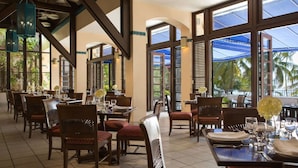 A restaurant with multiple tables and chairs, large windows, and a view of palm trees.