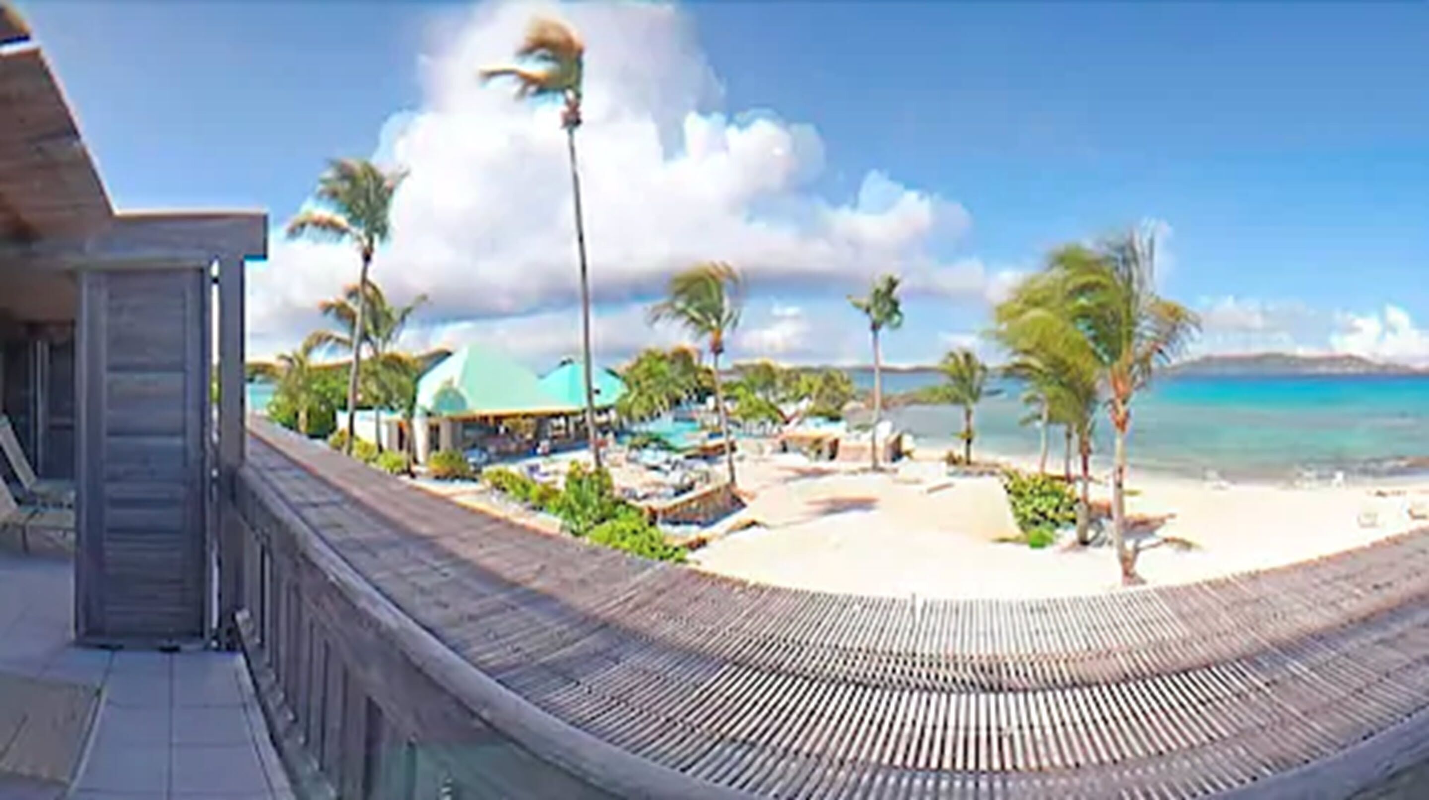Een strandresort met een houten terras, palmbomen en helder uitzicht op de oceaan.