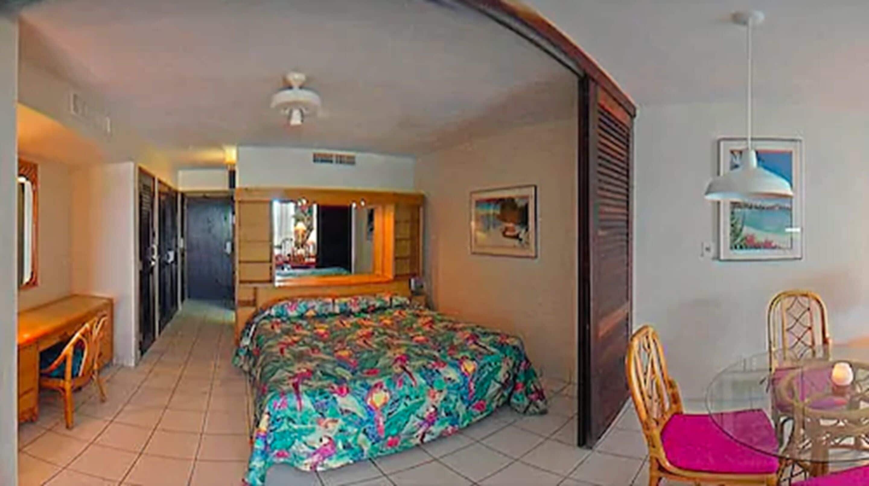 Een hotelkamer met een bed, een bureau, een stoel, een eettafel en een plafondventilator.