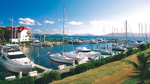 A marina with multiple boats docked, a building with a red roof, and a clear blue sky. - Sapphire Beach Resort (St. Thomas)