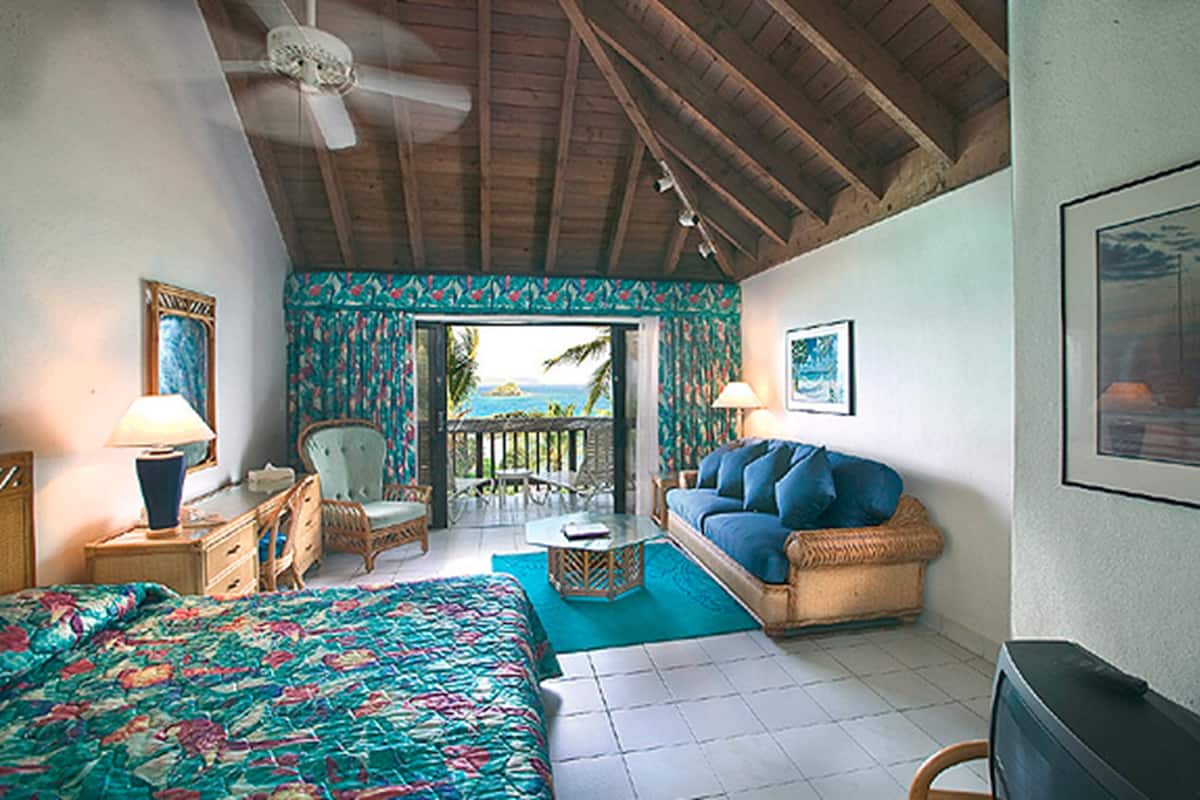 A room with a bed, a sofa, a chair, a table, and a view of the ocean through a door.
