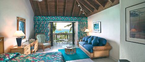 A room with a bed, a sofa, a chair, a table, and a view of the ocean through a door.