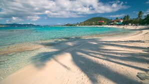 A beach with clear turquoise water, sandy shore, and a few buildings in the background. - Sapphire Beach Resort (St. Thomas)