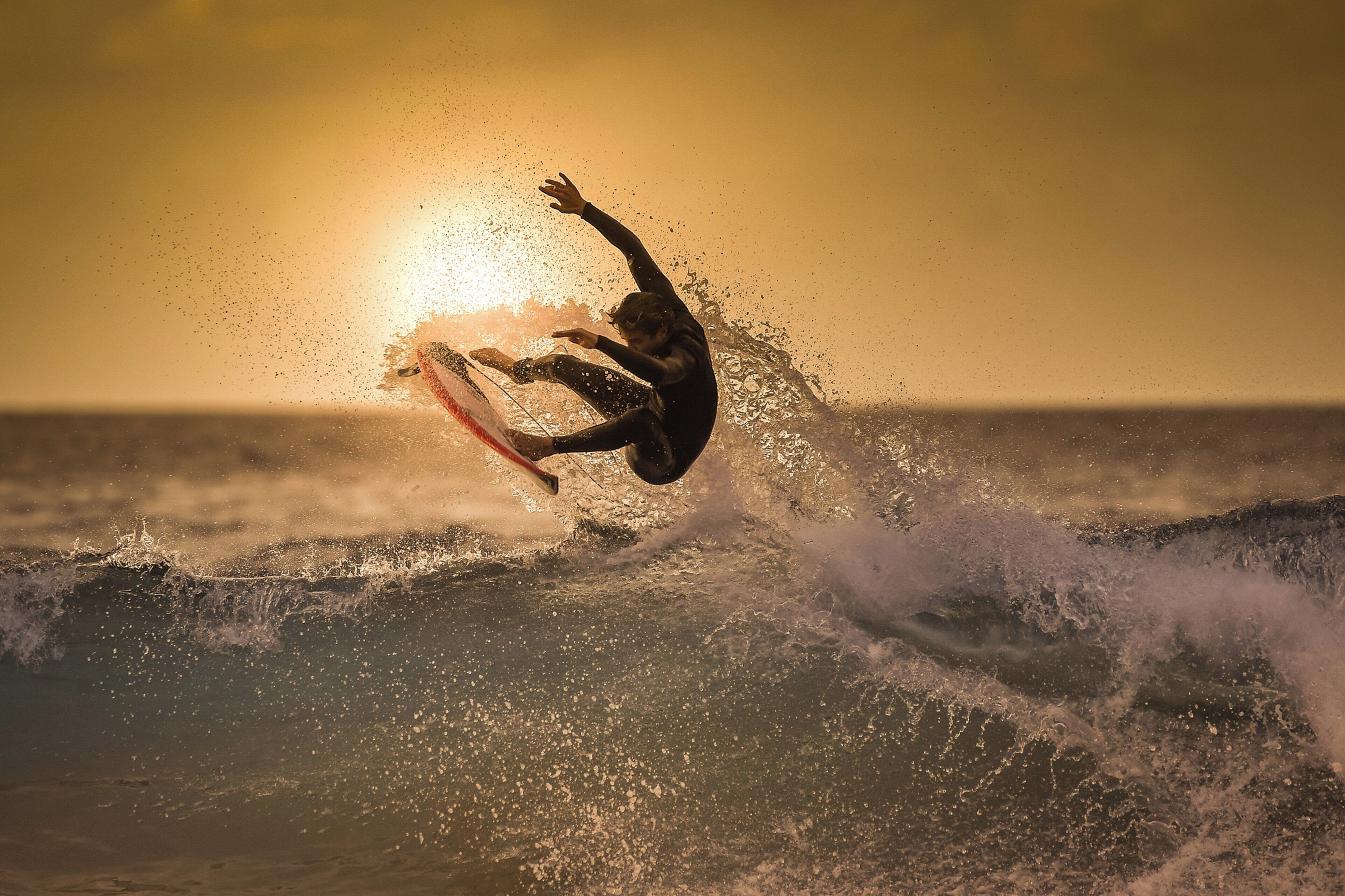 Un surfeur surfe sur une vague, avec le soleil couchant en arrière-plan.