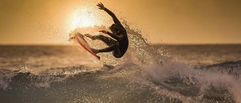 A surfer riding a wave with the sun setting in the background.