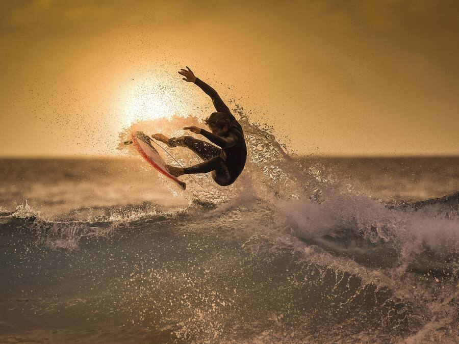 Un surfeur surfe sur une vague, avec le soleil couchant en arrière-plan.