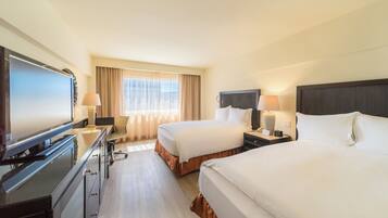 A hotel room with two beds, a desk with a computer, a TV, and a window with curtains.