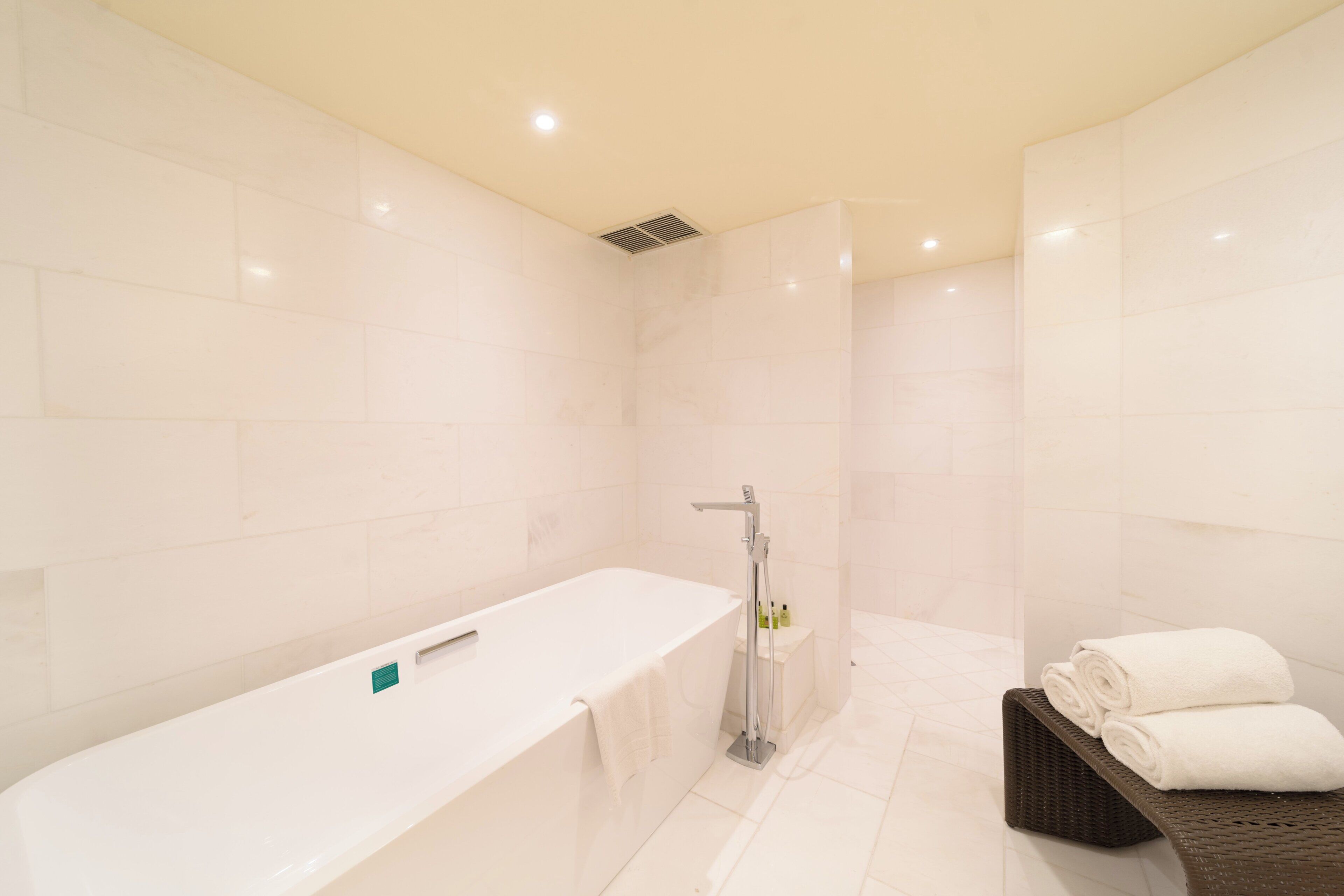 Une salle de bain moderne avec une grande baignoire blanche, un espace douche et un banc en osier avec des serviettes.