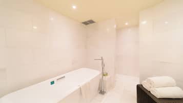 Une salle de bain moderne avec une grande baignoire blanche, un espace douche et un banc en osier avec des serviettes.