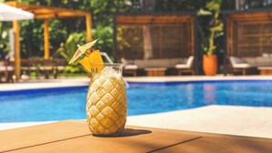 A glass with a textured pattern, possibly a drink, on a wooden table by a pool. - Real InterContinental San Salvador at Metrocentro Mall by IHG (San Salvador)