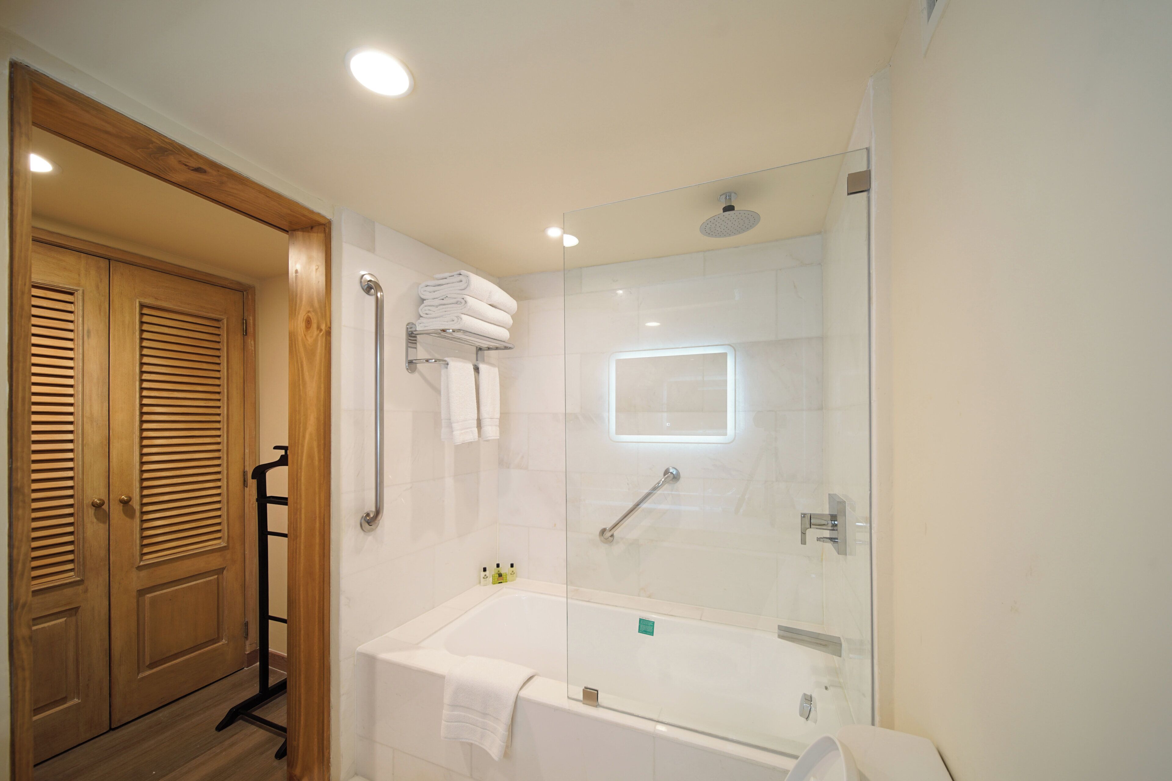 Un baño moderno con ducha envuelta en vidrio, una bañera blanca y puertas de madera.