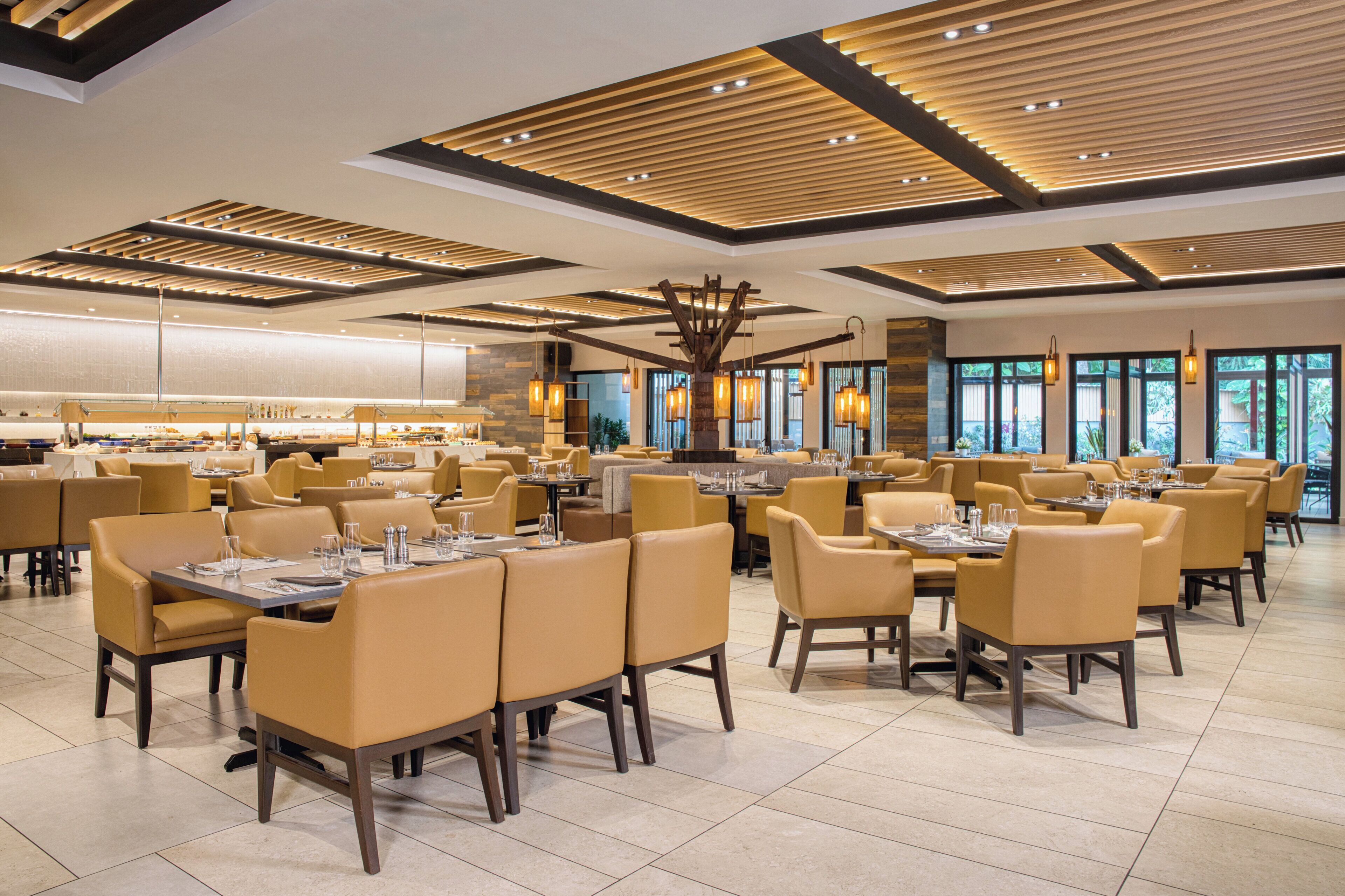 Un restaurante espacioso con varias mesas y sillas, un diseño de techo moderno y grandes ventanales que permiten la entrada de luz natural.