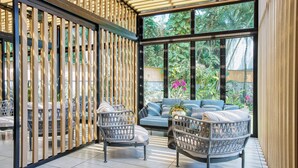 A sunlit room with a large window, wicker chairs, a blue sofa, and a wooden partition. - Real InterContinental San Salvador at Metrocentro Mall by IHG (San Salvador)