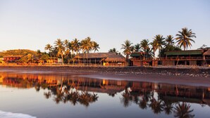 A beachfront hotel with palm trees, a thatched-roof structure, and a calm reflective water surface. - Real InterContinental San Salvador at Metrocentro Mall by IHG (San Salvador)