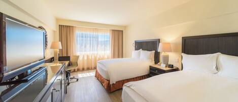 A hotel room with two beds, a desk with a television, and a window with curtains.