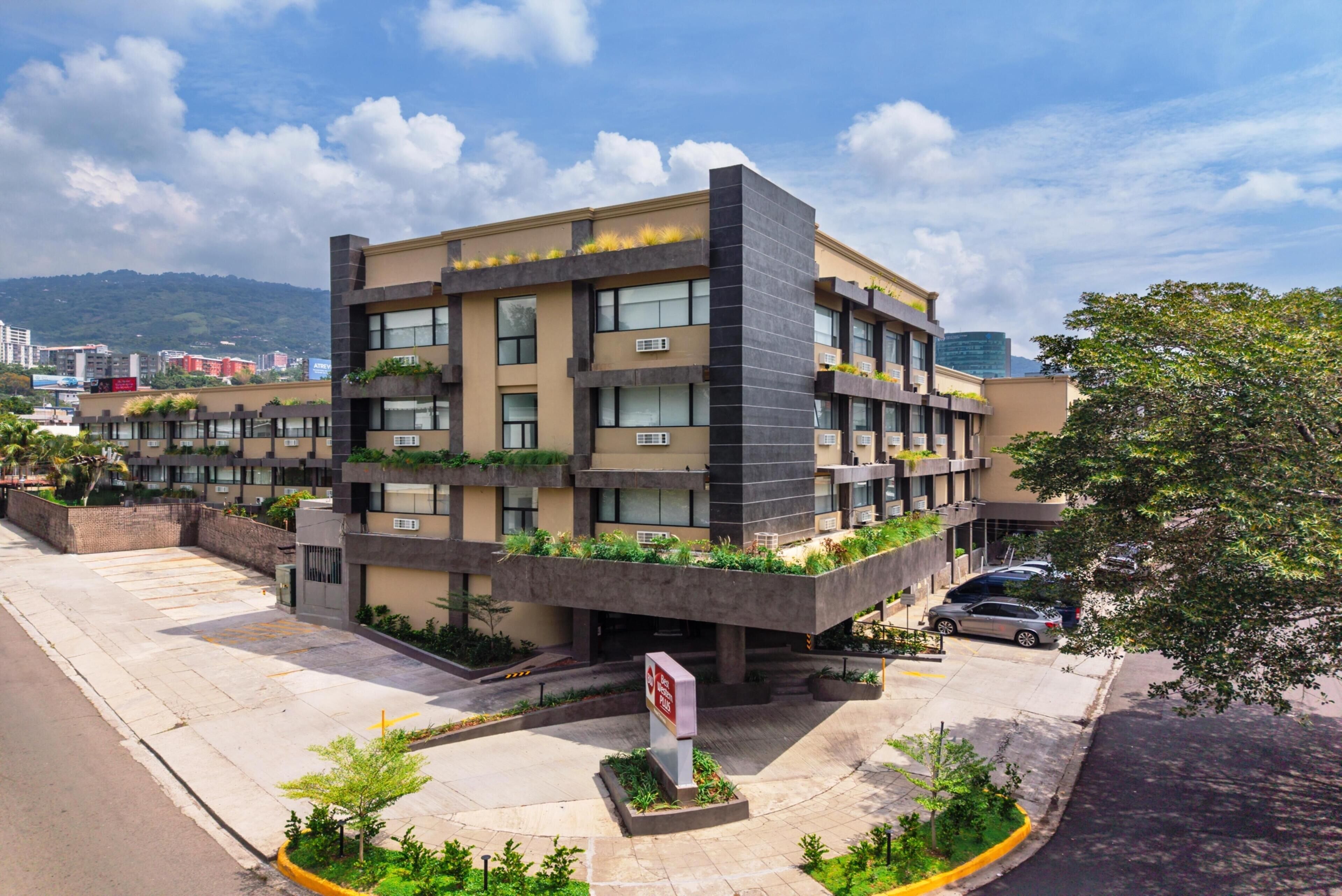 A multi-story building with a flat roof, large windows, and a parking area with a sign.