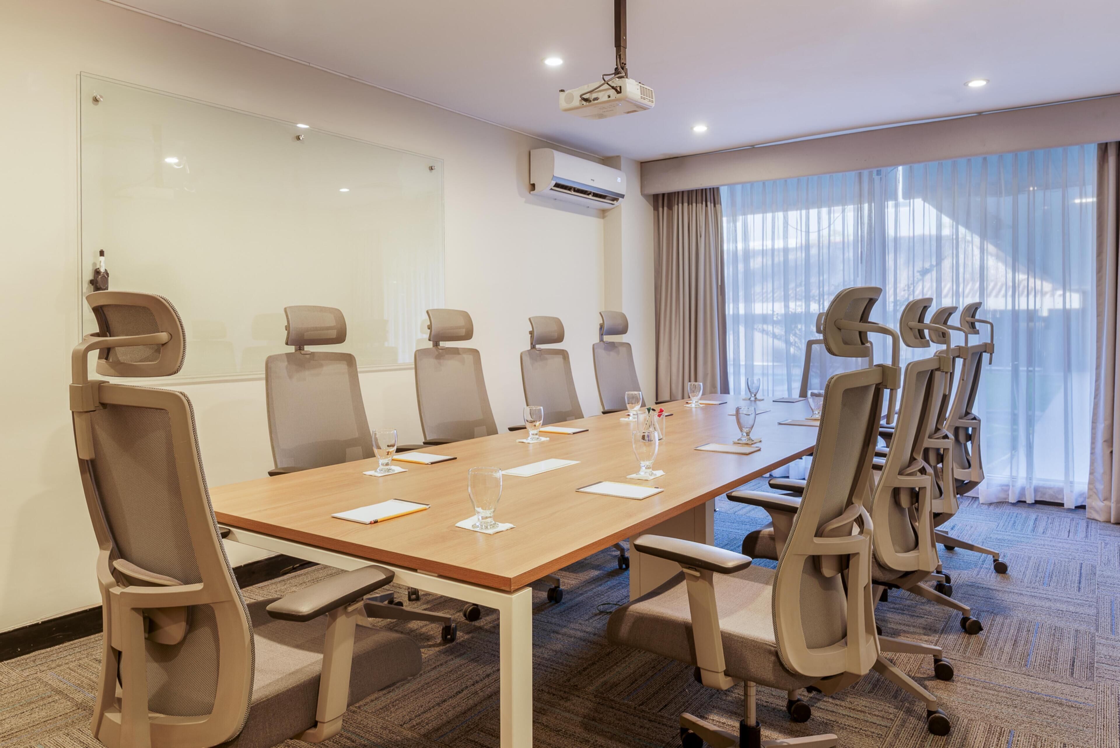 A conference room with a long table, multiple chairs, a whiteboard, and an air conditioning unit.