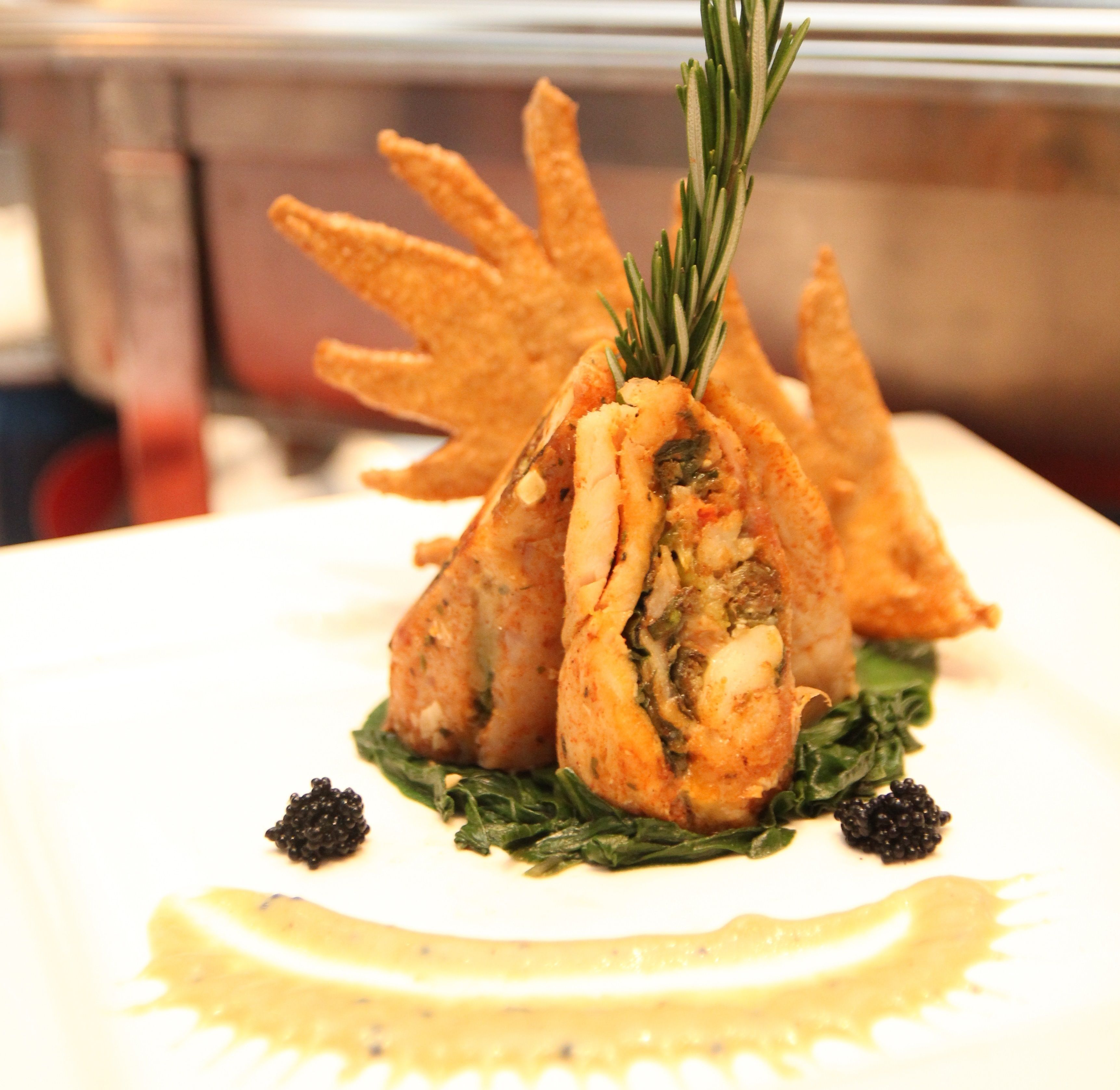 A dish with a sprig of rosemary on top, served on a white plate with a lemon wedge and black caviar.