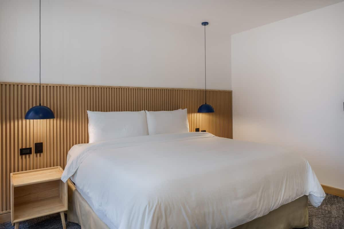 Un lit bien fait, avec une tête de lit en bois, deux lampes de chevet et une petite table de nuit en bois.