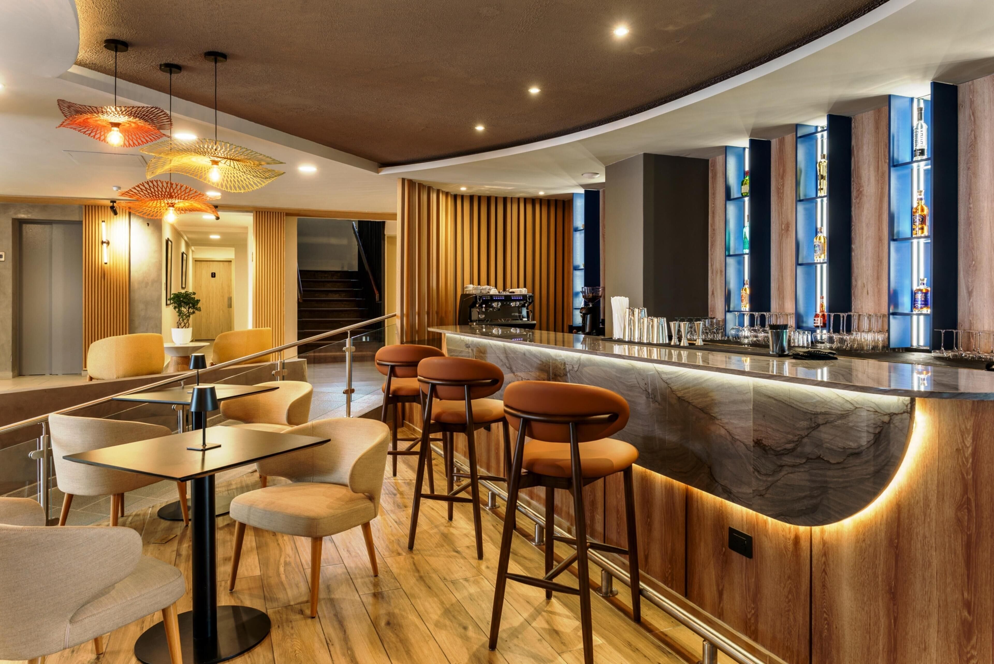 Een moderne bar met een marmeren aanrechtblad, houten details en barstoelen.