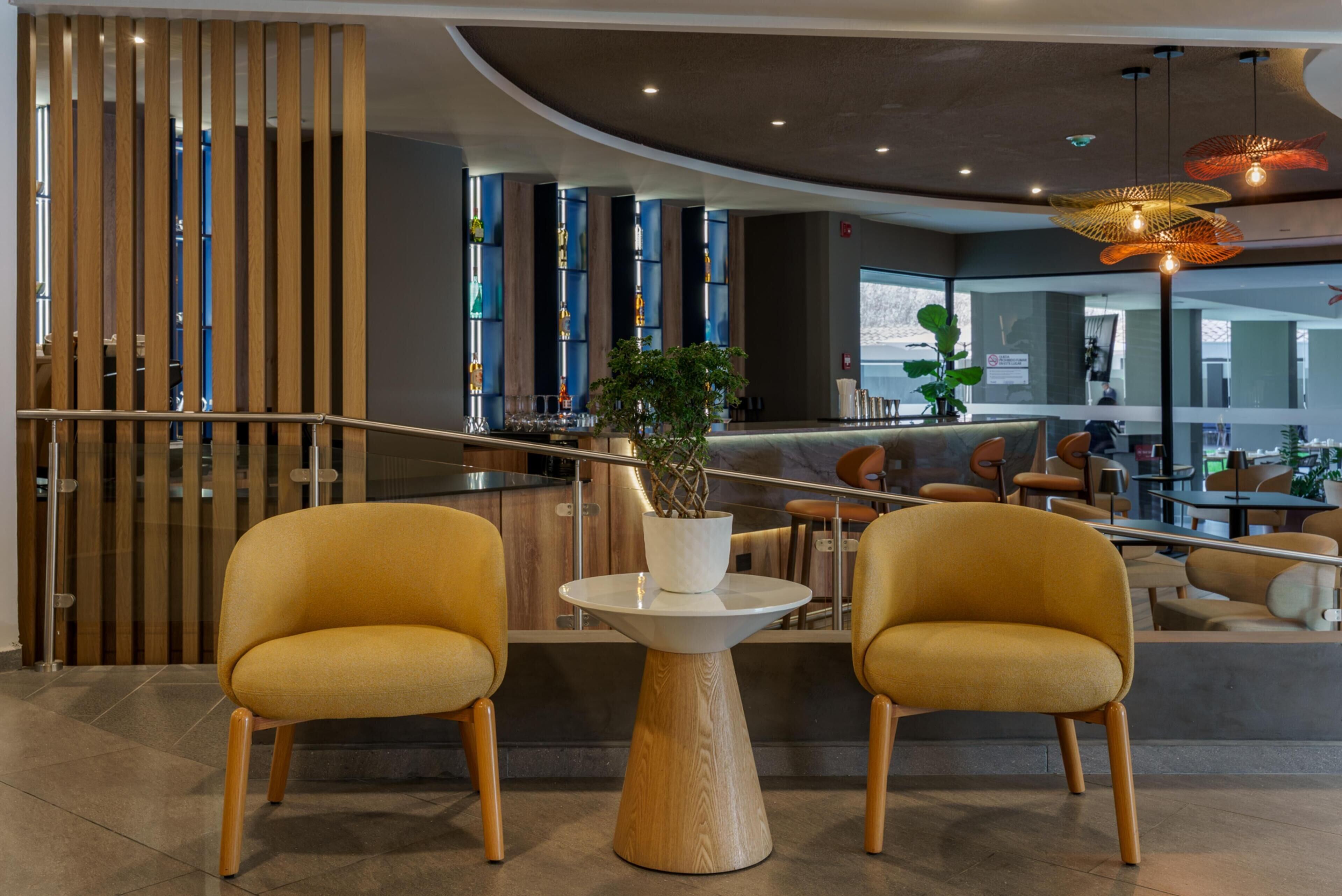 A modern interior with two yellow chairs, a wooden table, and a bar area with a plant centerpiece.