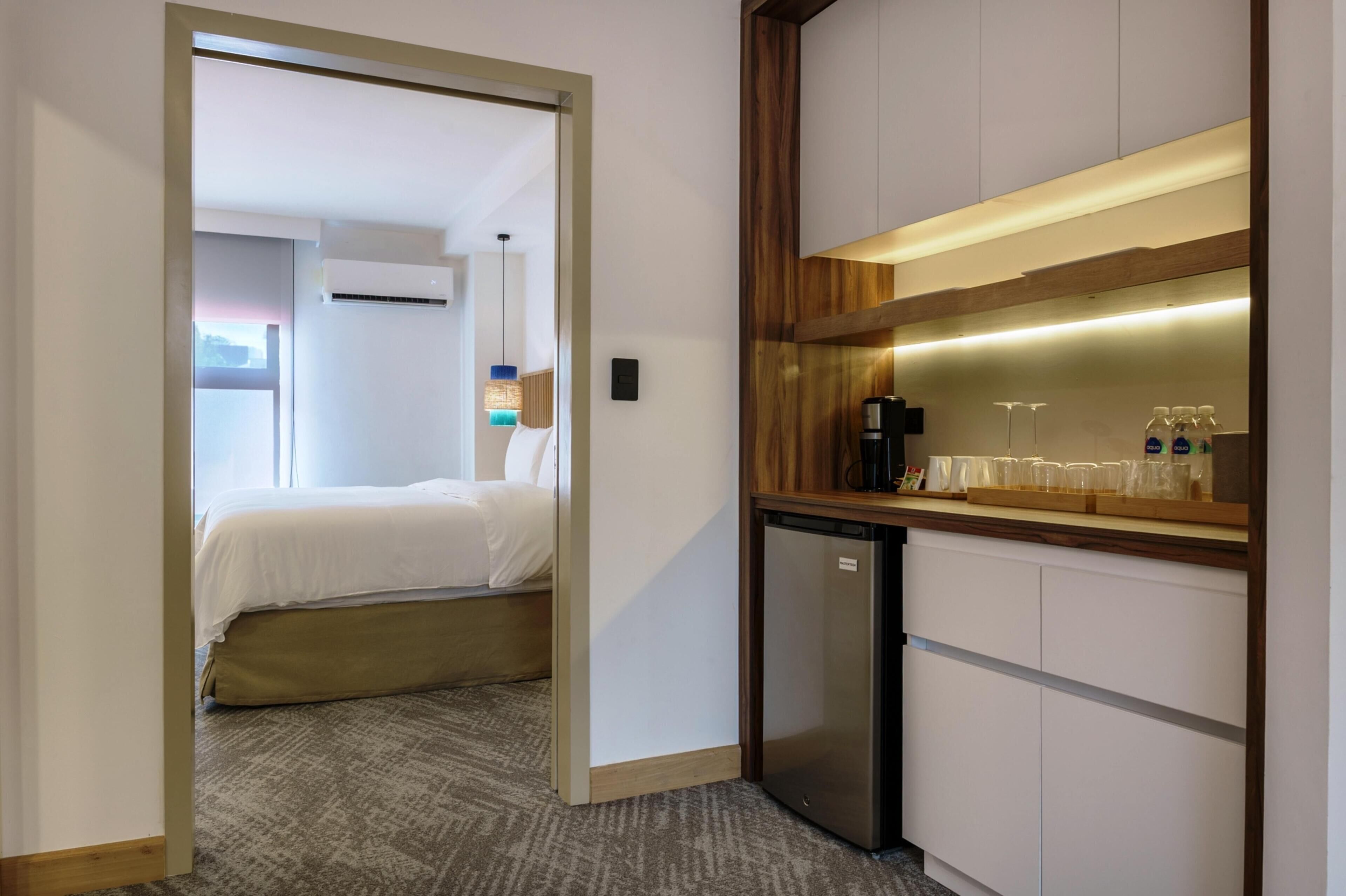 A hotel room with a bed, a kitchenette with a refrigerator, a coffee maker, and a microwave.