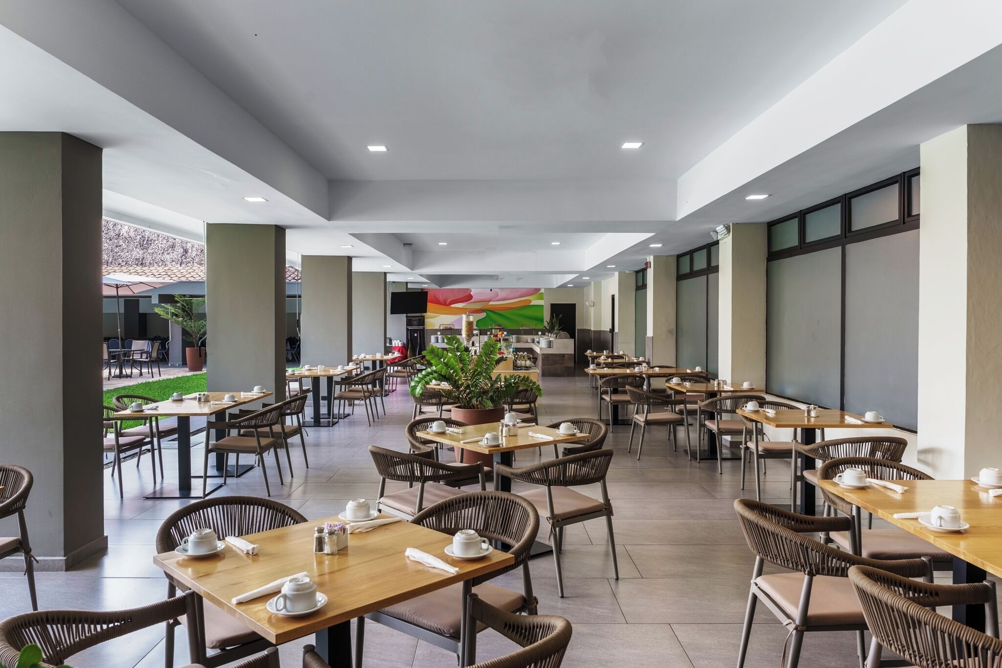 A spacious indoor dining area with multiple tables and chairs, a central plant, and a view of the outdoor patio.
