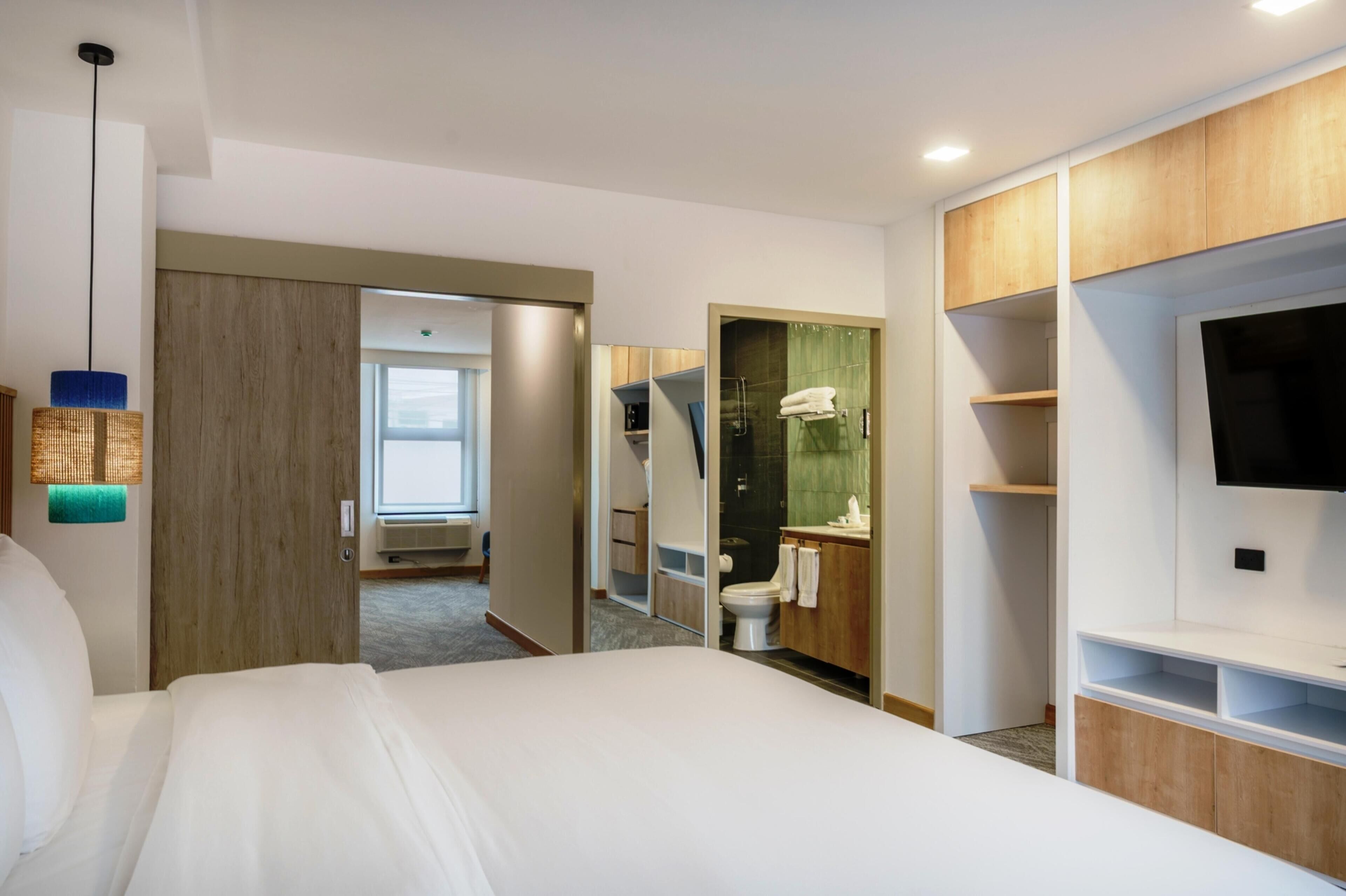 A hotel room with a bed, a TV, a bathroom with a shower, and a walk-in closet.