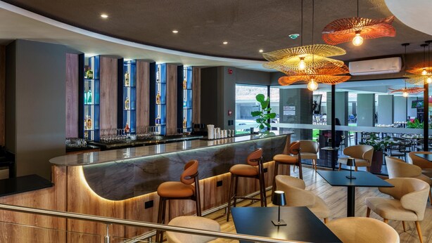 A modern bar area with a curved counter, bar stools, and pendant lighting. - Best Western Plus Hotel Terraza (San Salvador)