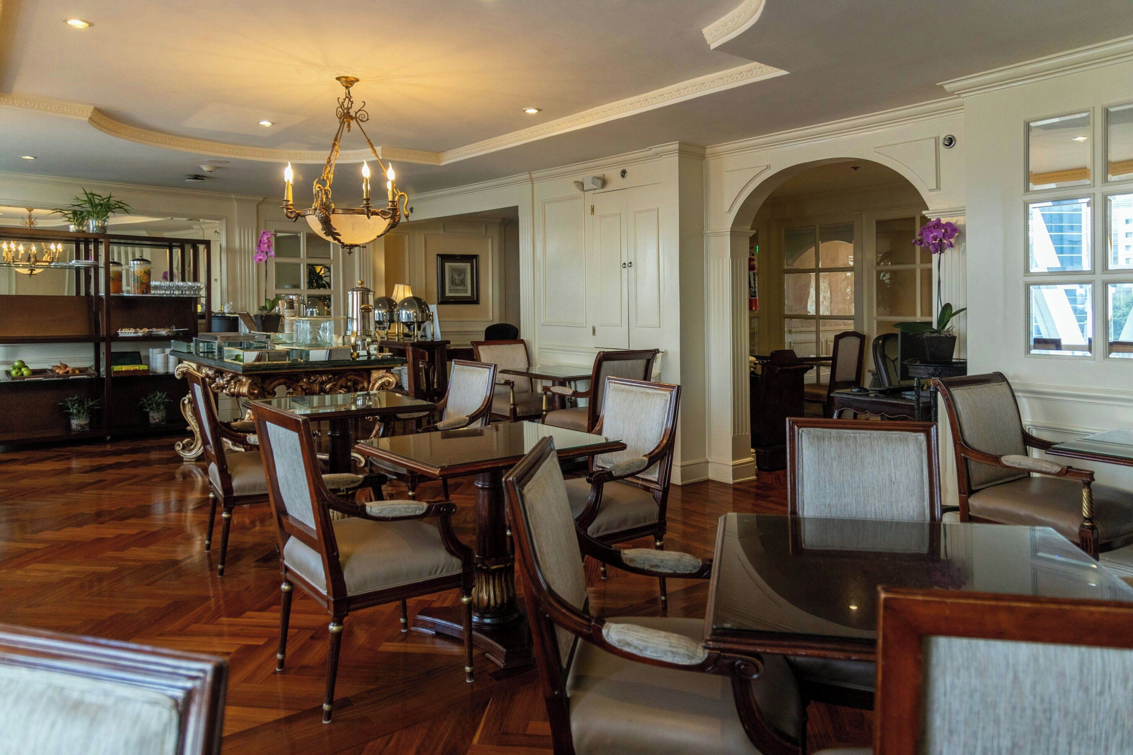 A spacious dining area with a chandelier, wooden furniture, and a view of the kitchen in the background.