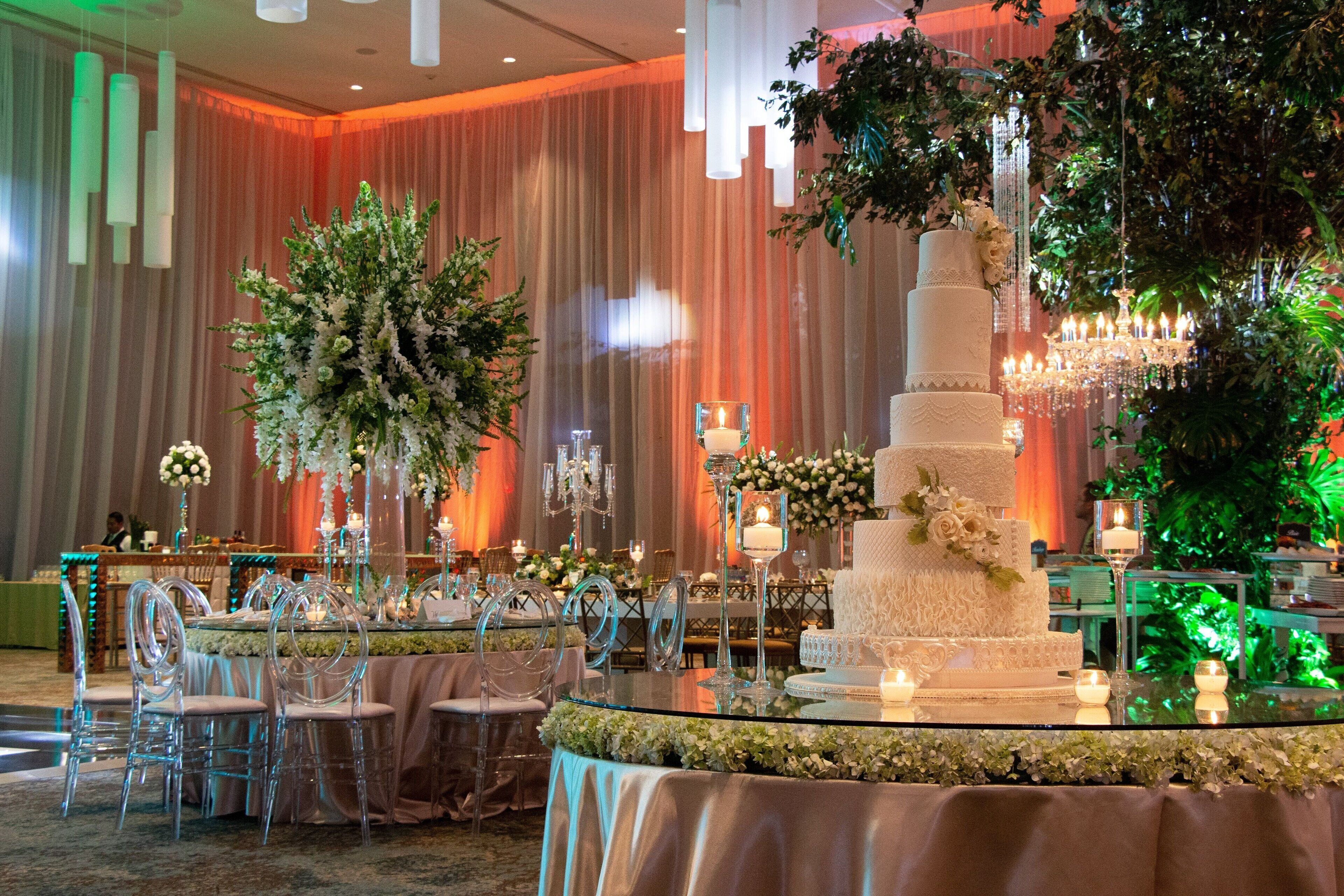 Un espace dédié à la réception de mariage, agrémenté d’un gâteau blanc à plusieurs étages, de compositions florales et d’un éclairage élégant.