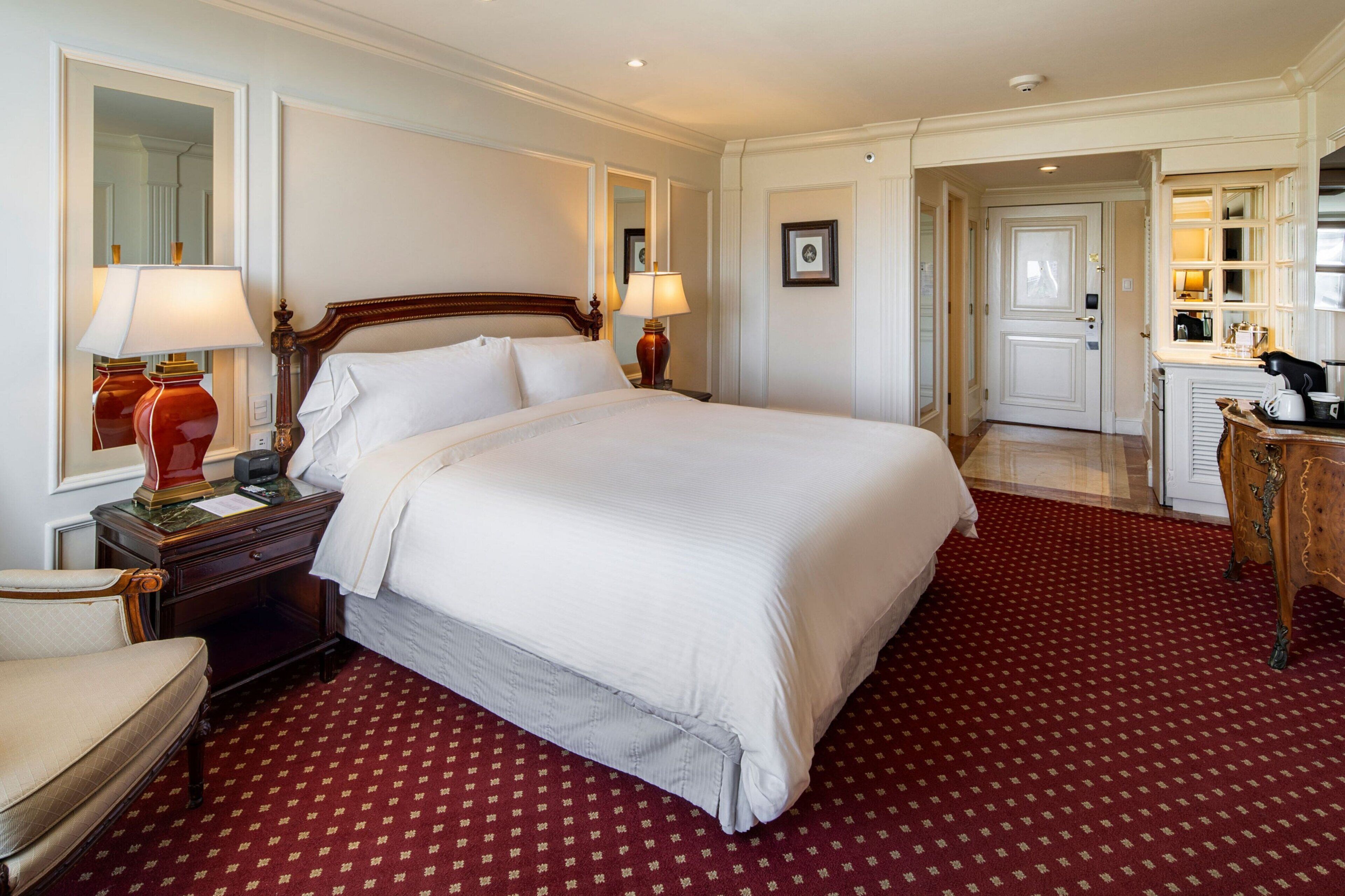A hotel room with a large bed, two bedside tables with lamps, a chair, and a desk with a mirror.