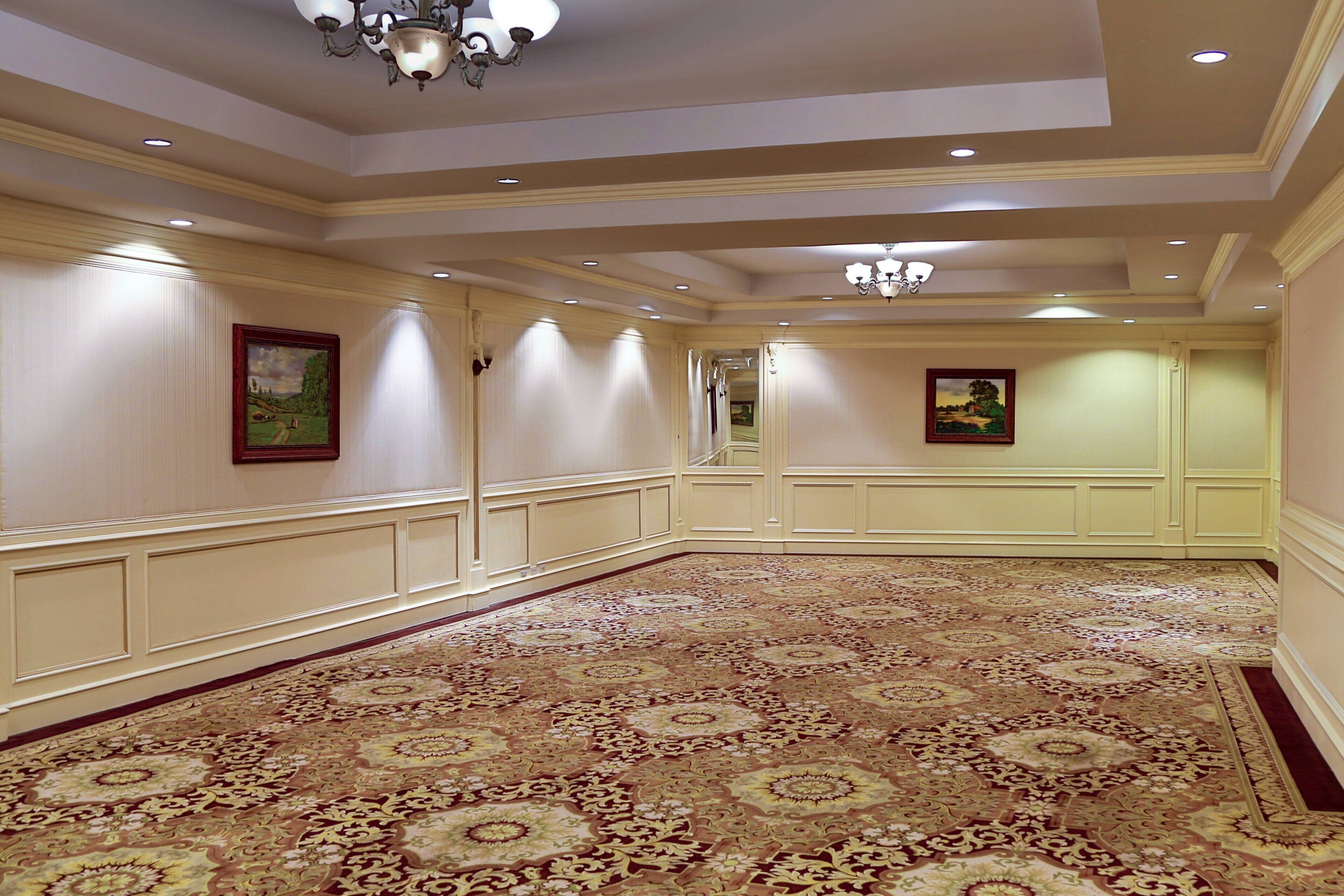 A spacious hallway with a patterned carpet, cream-colored walls, and recessed lighting.
