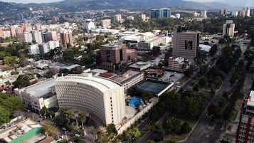 Paisagem urbana com um edifício curvo imponente e uma cúpula, cercado por outros arranha-céus, ruas e áreas verdes.