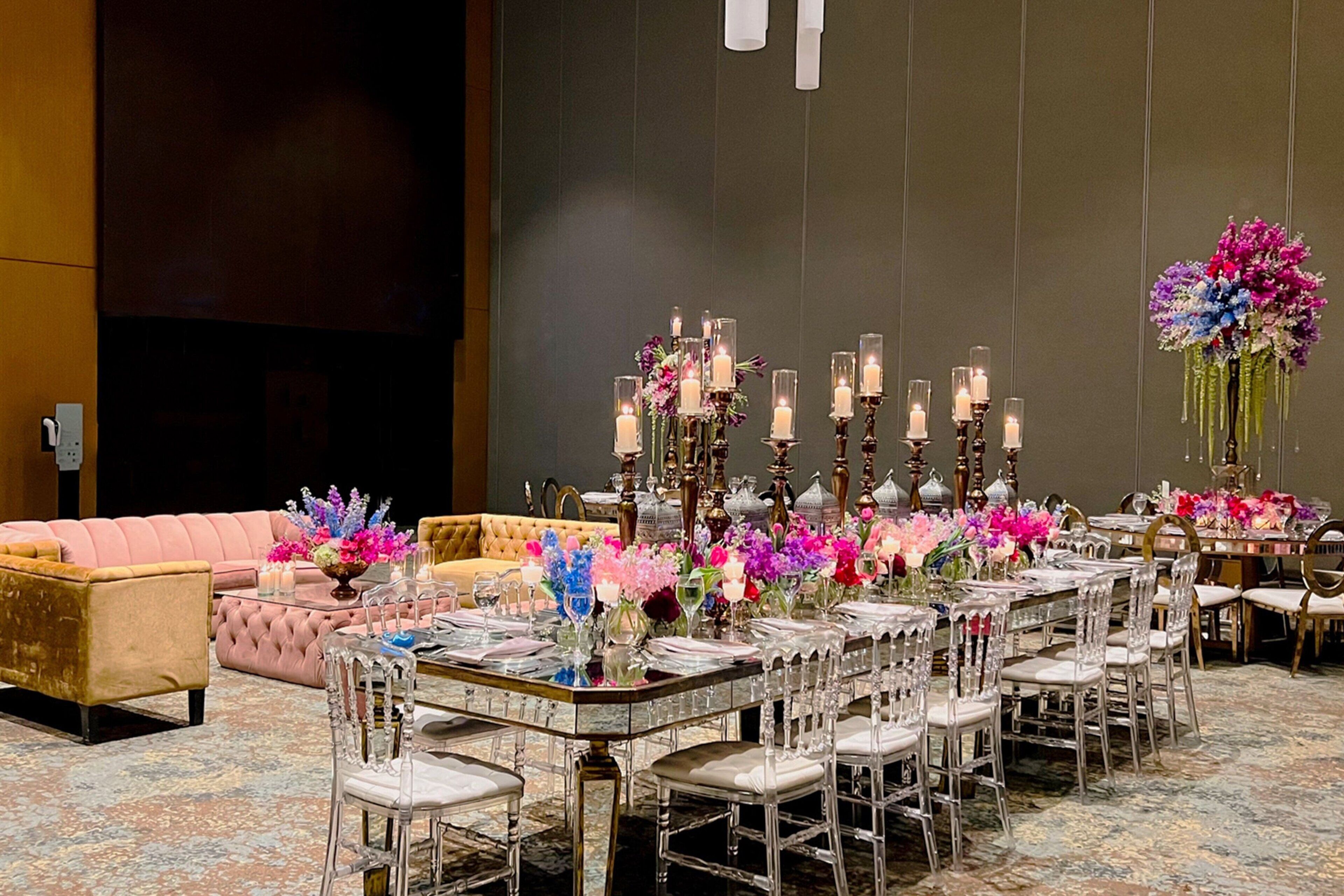 Un comedor formal con una larga mesa dispuesta para varios invitados, rodeada de sillas transparentes y decorada con arreglos florales y velas.