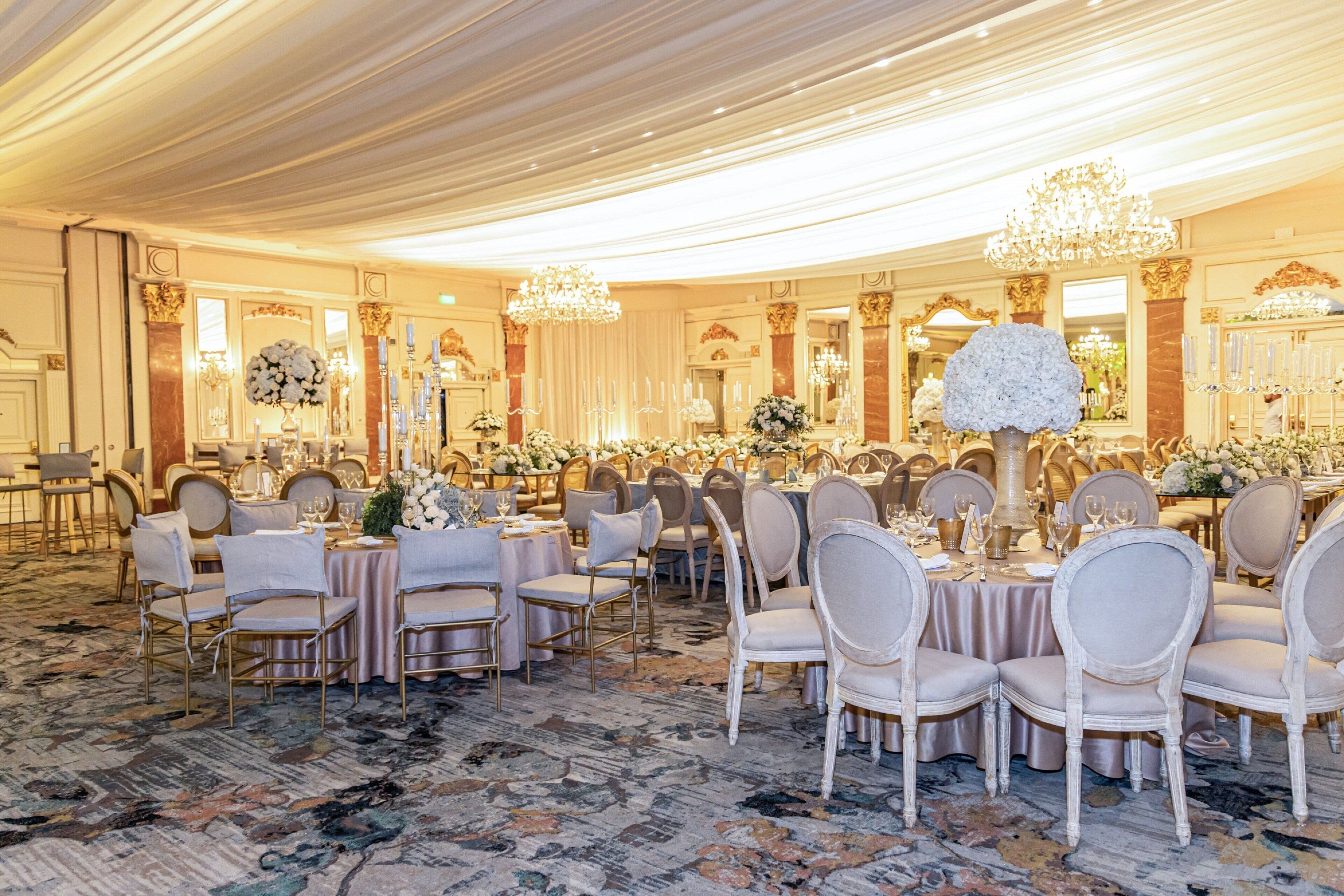 Une salle de banquet avec des tables rondes, des chaises, des lustres et des décorations florales.