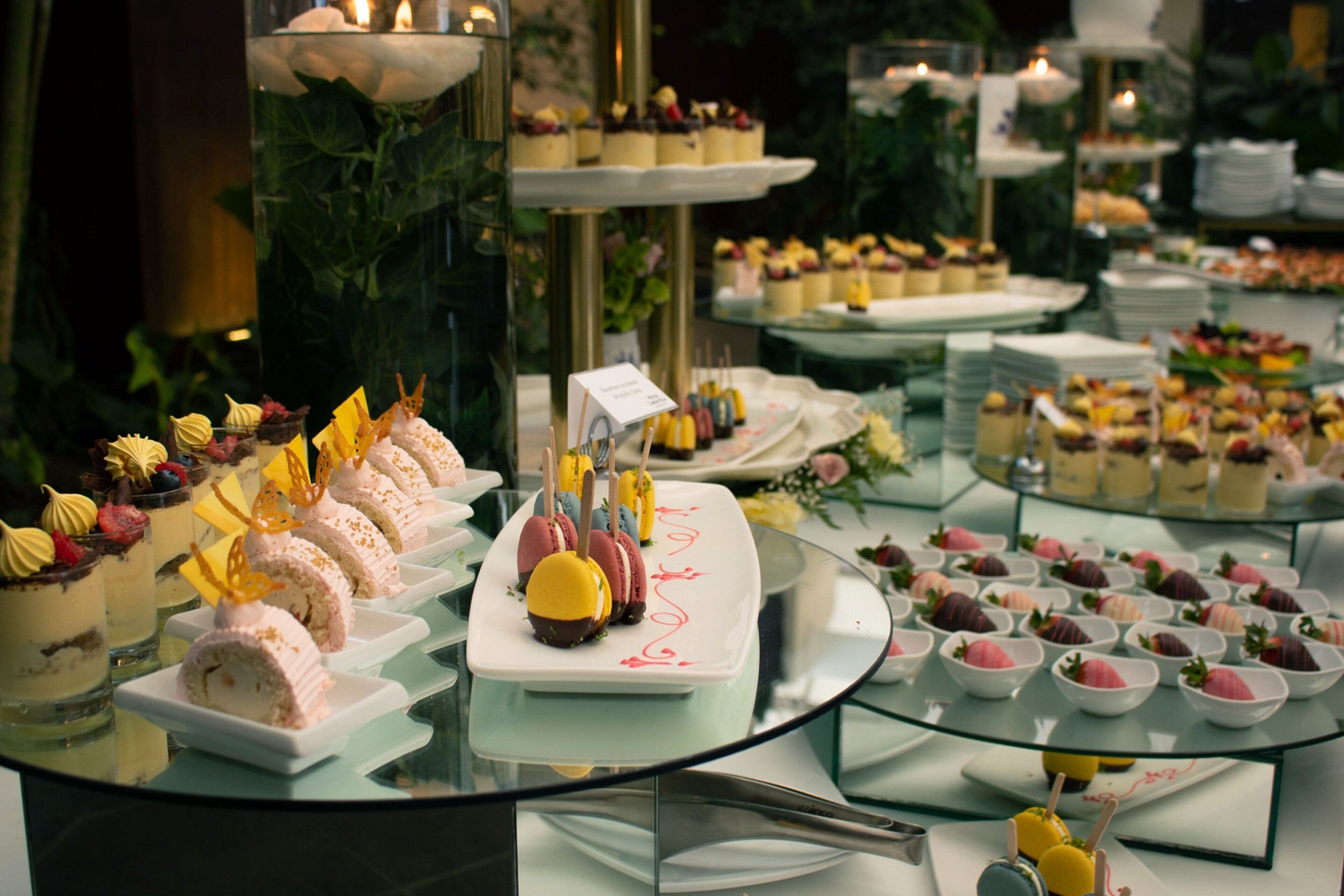 A buffet with various desserts and snacks arranged on glass tables.