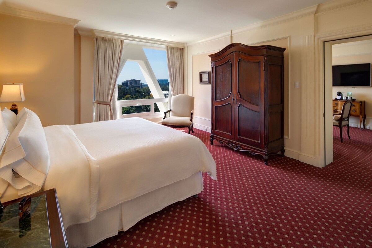 Habitación de hotel con una cama grande, un armario, una silla y un televisor.