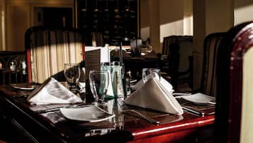 A dining table set with plates, glasses, and cutlery, with a wine glass and a bottle visible.