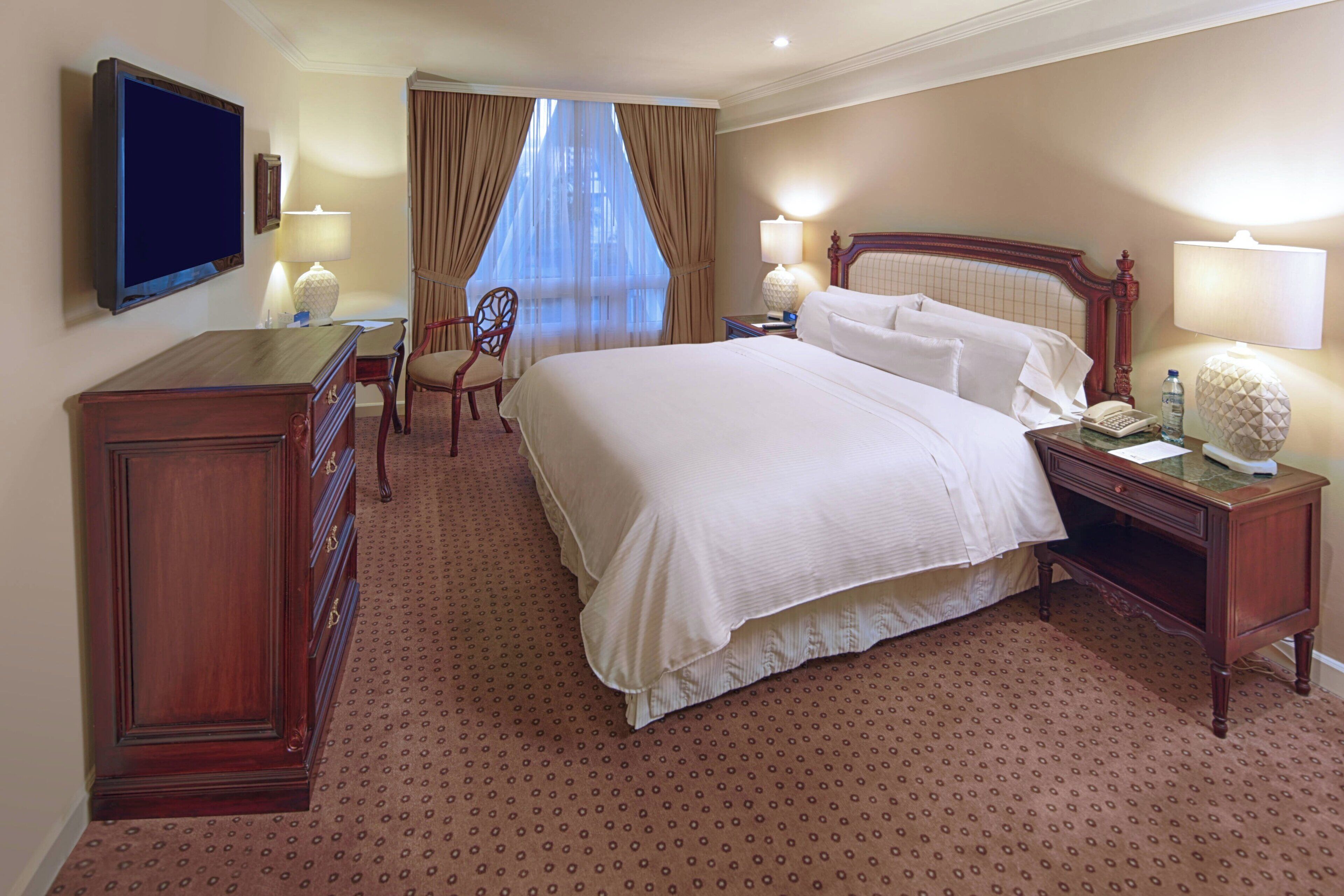 Una habitación de hotel con una cama grande, un escritorio con una silla, un televisor y una lámpara.