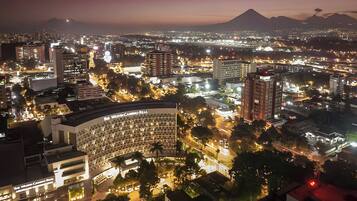 Un paisaje urbano nocturno con edificios iluminados, incluyendo un hotel destacado de fachada circular y varios pisos.