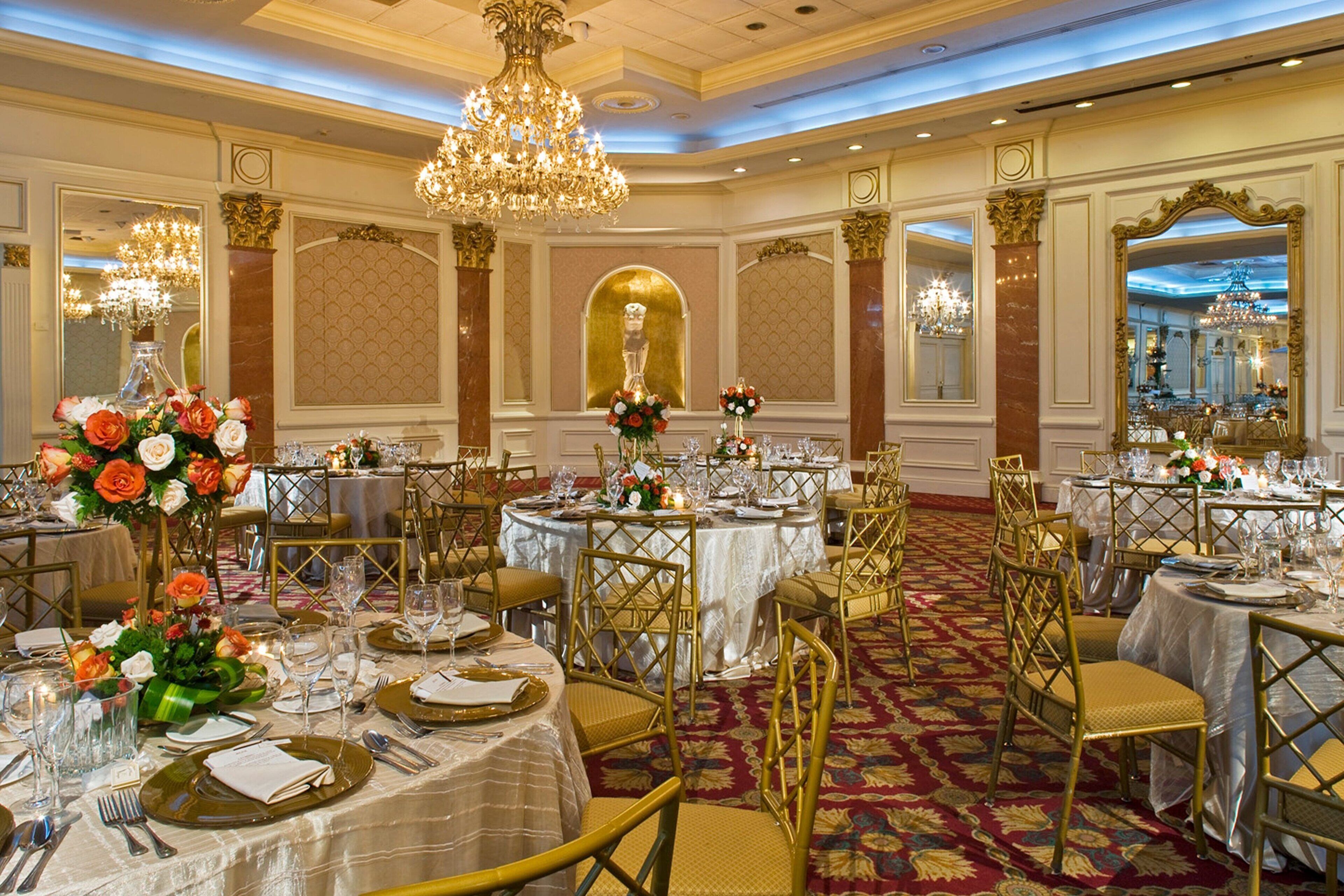 Une salle de banquet avec des tables rondes, des chaises dorées, des lustres et des compositions florales en guise de décoration de table.