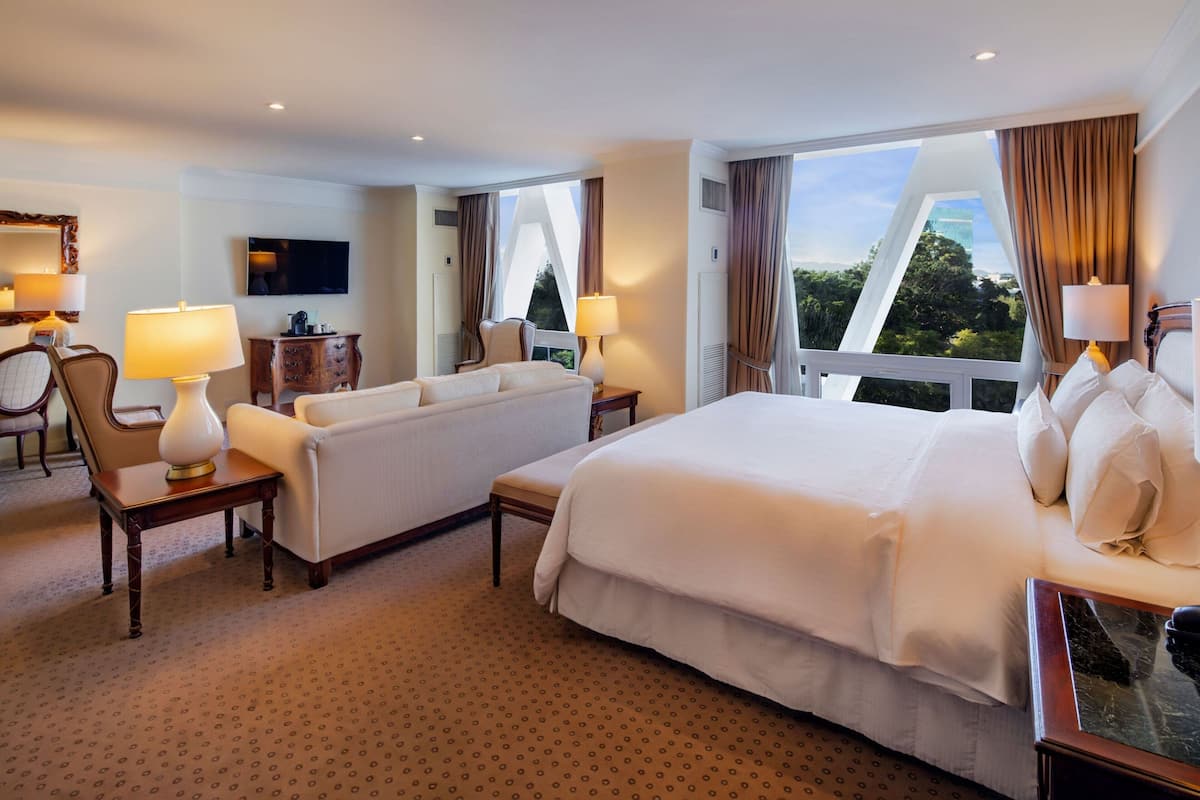 A hotel room with a large bed, a sofa, a desk, and a TV.