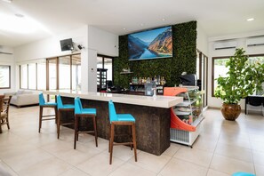 Zona de bar moderna con una gran pantalla de televisión, taburetes, una barra y una planta en maceta.