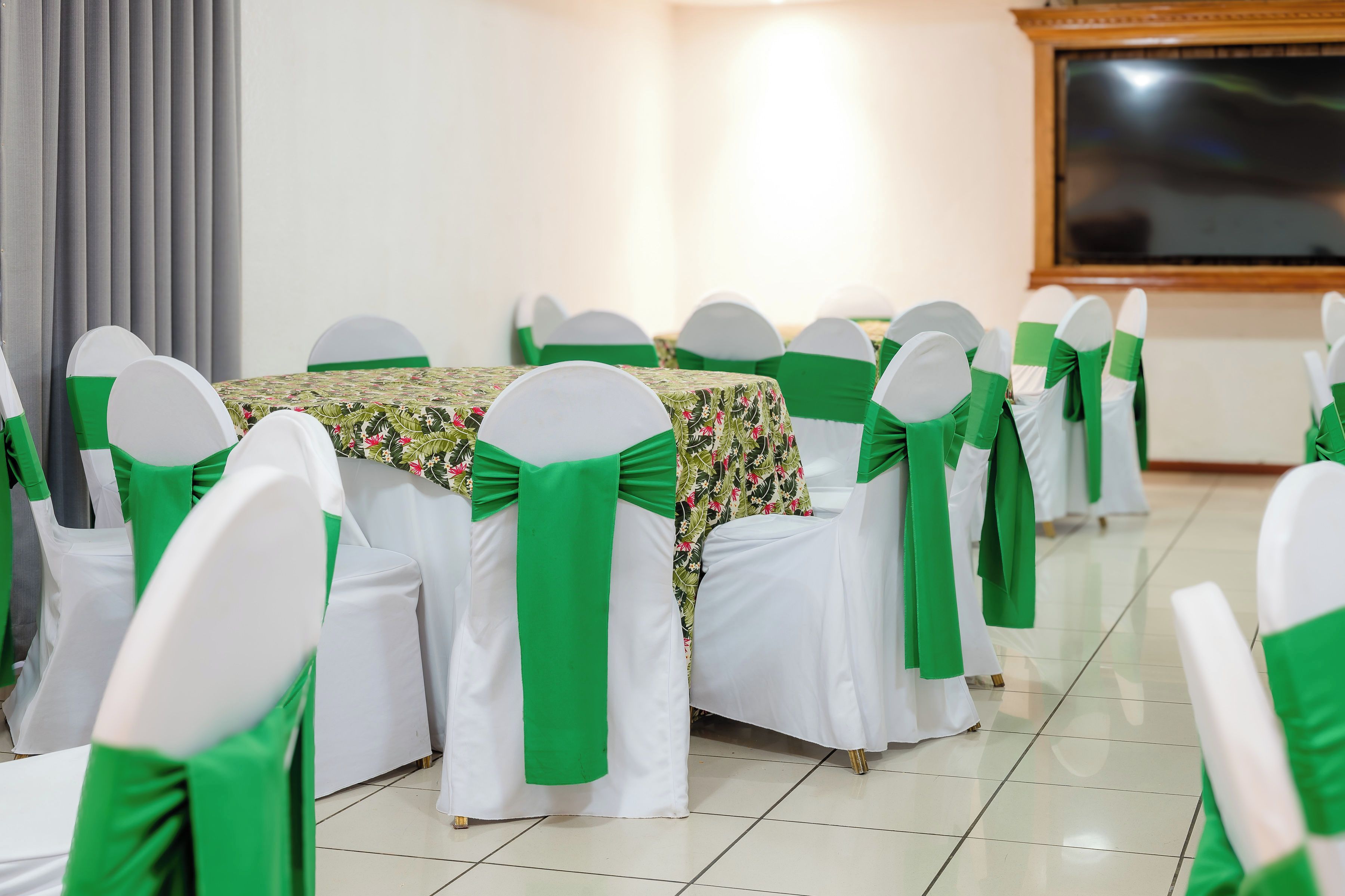 Un salón de conferencias con filas de mesas, cada una con mantel blanco y adornos verdes.