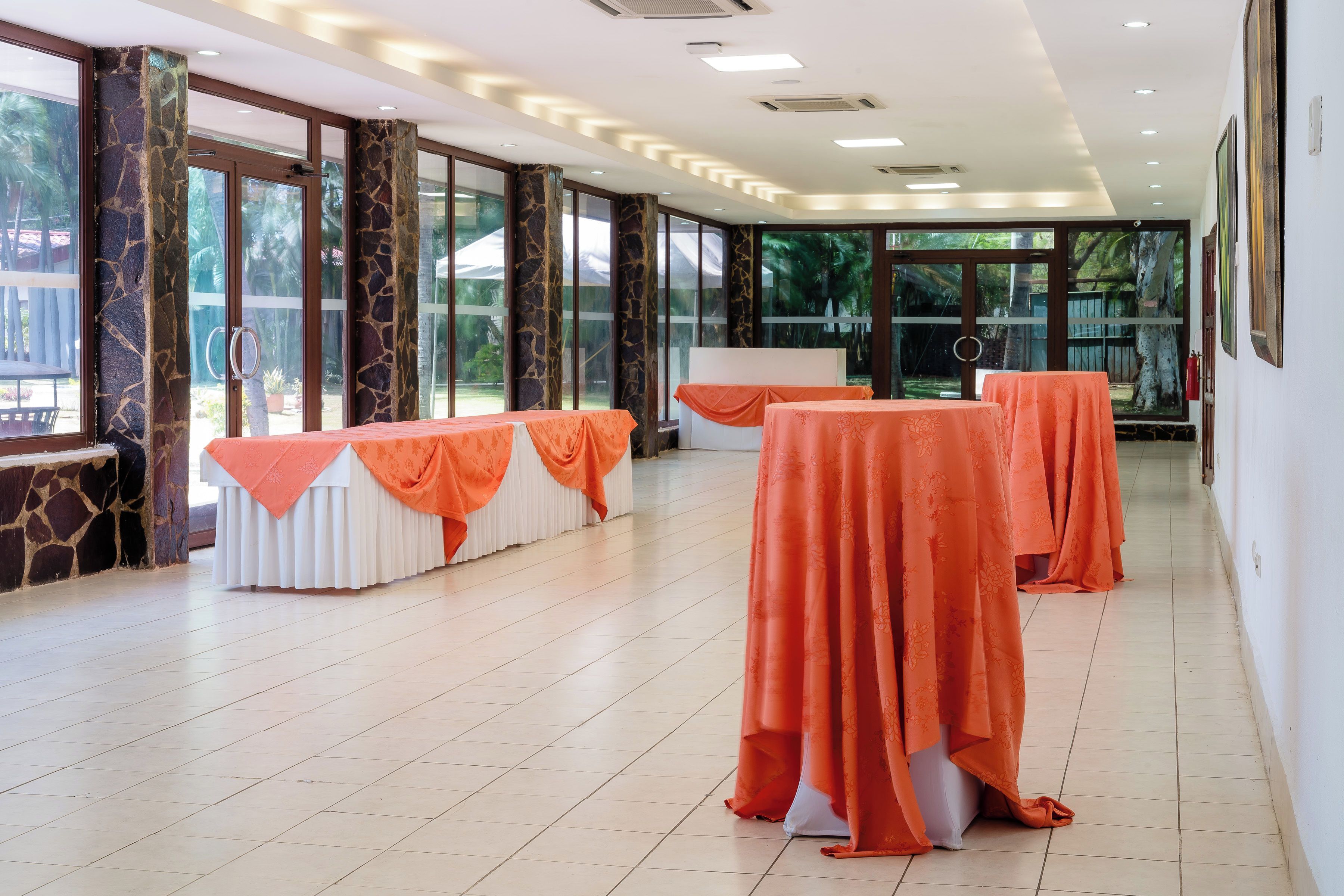 A spacious indoor area with large windows, a white table with an orange tablecloth, and a whiteboard.
